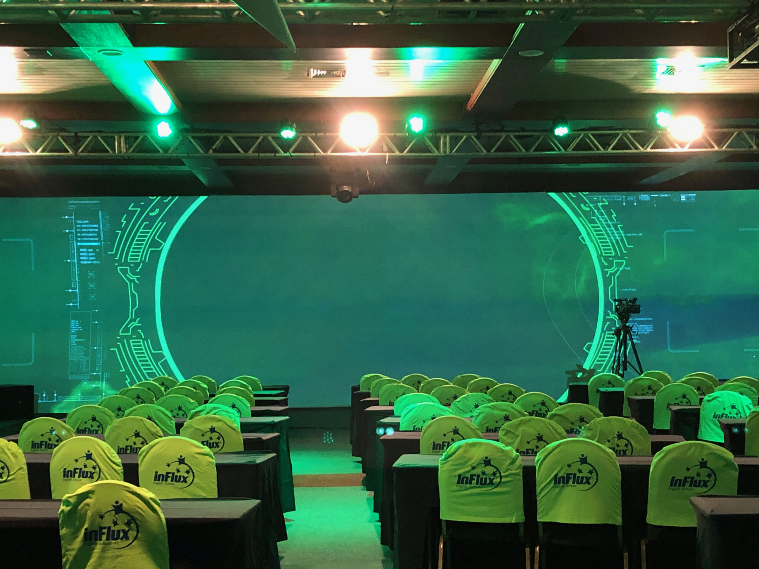 Montagem de Auditório Personalizado com Cenografia Circular de LED – Upgrade Rental Auditório montado para evento corporativo, com cadeiras personalizadas e cenografia de fundo em LED com formato circular e iluminação verde.