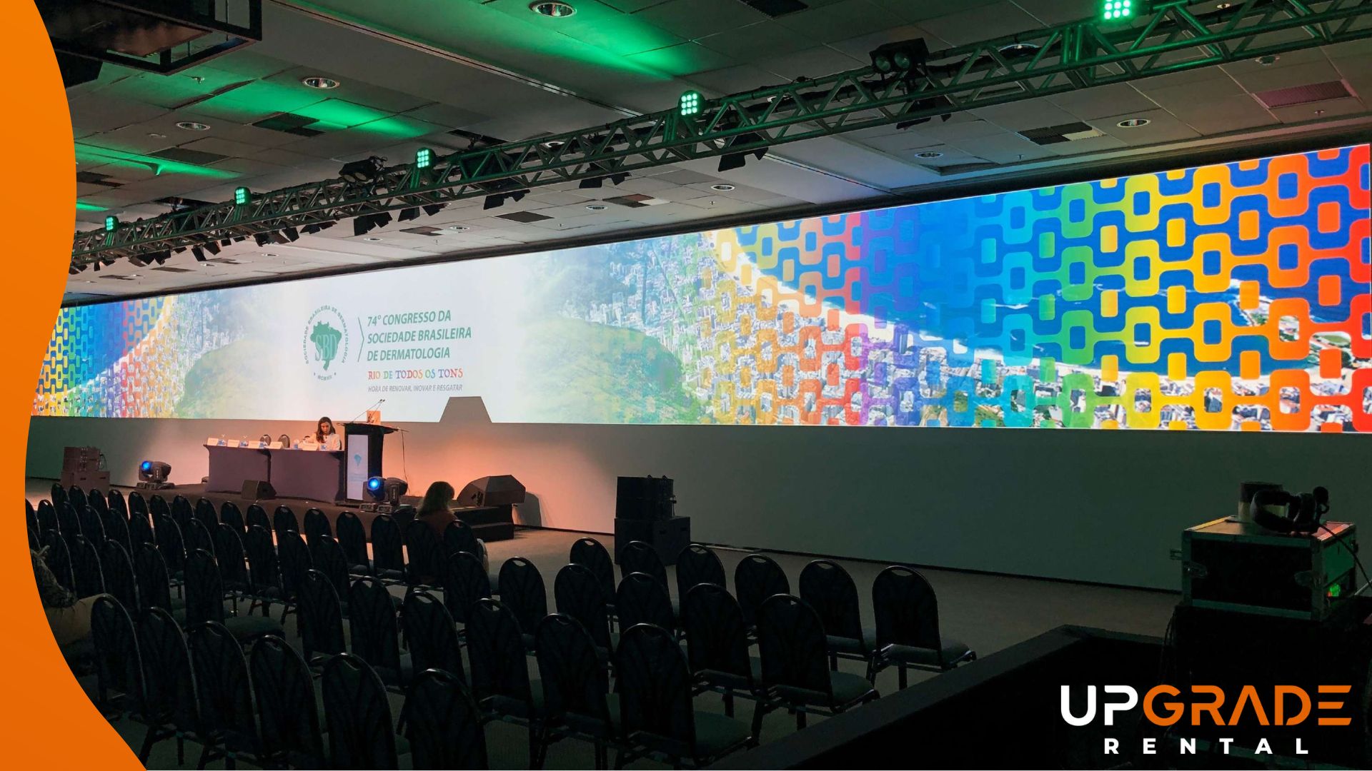 Sala de congresso montada com palco, mesa de palestrantes e tela de projeção panorâmica em alta resolução, trabalho da Upgrade Rental.